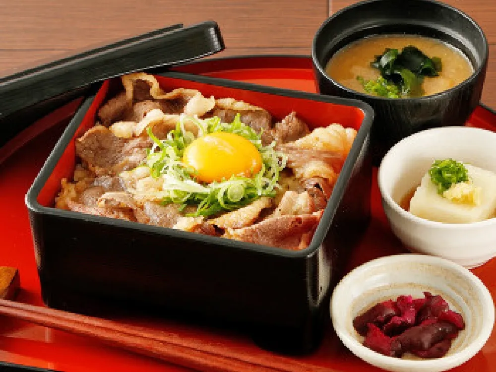 店舗限定メニュー「牛すき焼き重御膳」A representative course menu at restaurants in western Japan: “Gyusukiyaki Gozen (beef sukiyaki rice bowl set meal)” The menu includes:Small side dish,Gyusukiyaki (beef sukiyaki rice bowl),Miso soup,Pickles